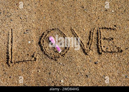 Zeitlose Liebe: „Liebe“ am Strand in einer rosafarbenen Sanduhr, wo Romantik auf den Sand ewiger Momente trifft Stockfoto