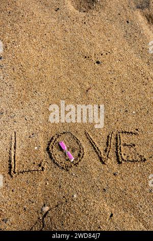 Zeitlose Liebe: „Liebe“ am Strand in einer rosafarbenen Sanduhr, wo Romantik auf den Sand ewiger Momente trifft. Stockfoto