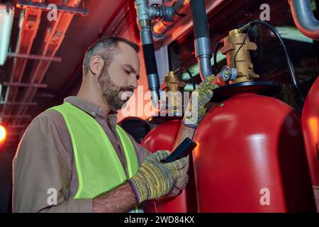 Gut aussehender, hingebungsvoller Techniker in Sicherheitskleidung, der den Detektor während der Arbeit im Rechenzentrum verwendet Stockfoto