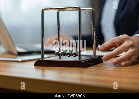 Ein reifer Geschäftsmann im Anzug interagiert mit der Wiege eines Newton auf seinem Schreibtisch und symbolisiert die Entscheidungsfindung und Konzentration. Stockfoto