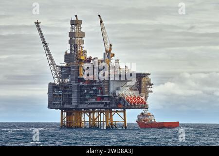 Nahaufnahme der Offshore-Plattform zum Aufbocken von Öl und Gas mit Versorgungsschiff, das an sonnigen Tagen im Meer Fracht betreibt. Stockfoto