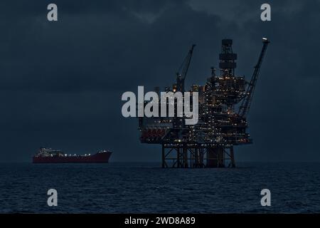 Nahaufnahme des beleuchteten Bohrgeräts und des schwimmenden Lagertankers für die Produktion bei Nacht im Ozean. Stockfoto