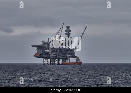 Versorgungsschiff, das Ladungsoperationen mit Aufbock-Bohrgerät durchführt, Offshore-Plattform in der Nordsee, mit grauem Himmel und Meer. Stockfoto