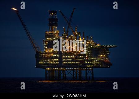 Nahaufnahme der beleuchteten Bohranlage bei Nacht mit dunkelblauem Himmel im tiefblauen Ozean. Stockfoto