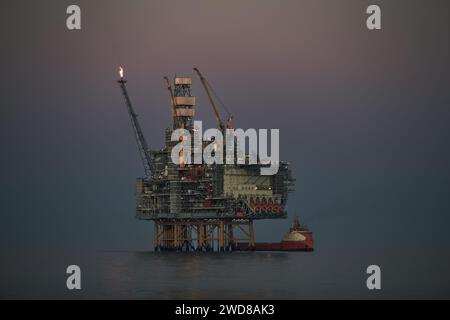 Nahaufnahme der Offshore-Öl- und Gasförderplattform, während des Frachtbetriebs mit Versorgungsschiff im Meer, während des wunderschönen bunten Sonnenuntergangs und ca. Stockfoto