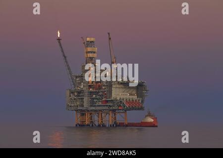 Panoramablick aus nächster Nähe auf die Offshore-Öl- und Gastankplattform, während Frachtbetrieb mit Versorgungsschiff im Meer, während der wunderschönen bunten Sonne Stockfoto