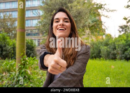 Porträt Junge Frau, die mit Daumen nach oben zeigt und draußen lächelnd in die Kamera blickt Stockfoto