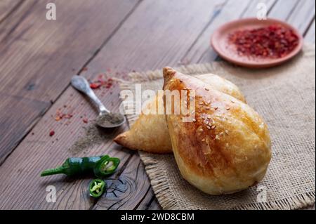 Köstlicher usbekischer Samsa mit Lamm und Gewürzen, die in Tandoor auf hölzernem Hintergrund gekocht werden. Usbekische und zentralasiatische Küche concept.jpg Stockfoto