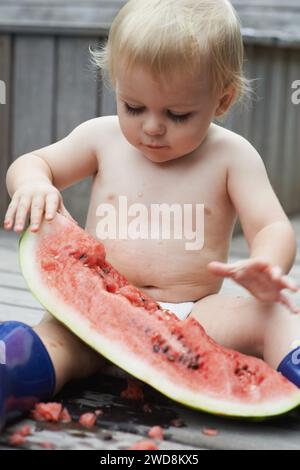 Baby, spielt mit Wassermelone und Essen, Hinterhof und Entwicklung mit Wachstum, Neugier und Zuhause. Kleinkind, Kind und Kleinkind im Garten, allein und Stockfoto