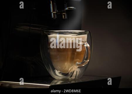 Heißer Kaffee mit Milch in Glasbecher isoliert auf schwarzem Hintergrund Stockfoto