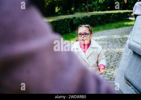 Porträt trauriges Down-Syndrom Mädchen in Brille, stehend vor ihrer unerkennbaren Mutter mit traurigem Gesicht, weinend und redend. Stockfoto