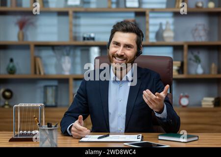 Erfahrener reifer Mann in Anzug und Headset, der von einem gut organisierten Home Office aus arbeitet und Selbstvertrauen und Charisma ausstrahlt. Stockfoto