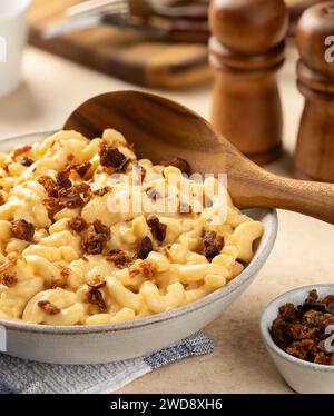 Makkaroni und Käse mit Speckstücken in einer weißen Servierschale und Holzlöffel Stockfoto