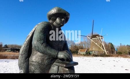 Amsterdam Niederlande 19. Januar 2024 Winterszenen in Amsterdam. Statue des niederländischen Malers Rembrandt van Rijn vor der Windmühle de Riekermolen entlang der Amstel mit Schneedecke und azurblauem Himmel. Schnee, Niesen, Weer, Wetter, Nässe, Standblende, schilder, Stockfoto