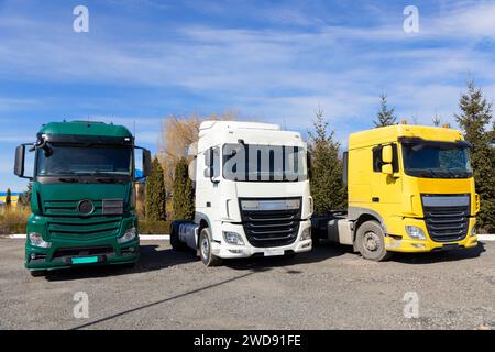 Drei Lkw parkten an einem sonnigen Tag hintereinander. Fahrerhäuser in verschiedenen Farben von Zugmaschinen-Anhängern. Stockfoto