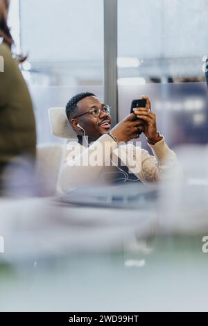 Männlicher Angestellter genießt Pause bei der Arbeit. Videos auf seinem Handy anschauen. Stockfoto