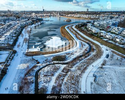 Dortmund, Nordrhein-Westfalen, Deutschland - Phoenix-See im Winter mit Schnee, vorne renaturierte Emscher. Der Fluss wurde zum naturnahem Gewaesser umgestaltet, Hochwasserschutz und Biodiversitaet durch neu gestaltete Ueberflutungsflaechen. Eine ehemalige Industriebrache von 99 Hektar Flaeche wurde zu Wohn-, Arbeits- und Freizeitflaechen und 24 Hektar Seeflaeche umgestaltet. Im Fall von Starkregenereignissen fungiert der See als Regenwasser-Rückhaltebecken. Die Emscher ist nach dem Bau eines parallel verlaufenden Abwasserkanals jetzt abwasserfrei, war vorher ein offener, oberirdischer Schmutz Stockfoto