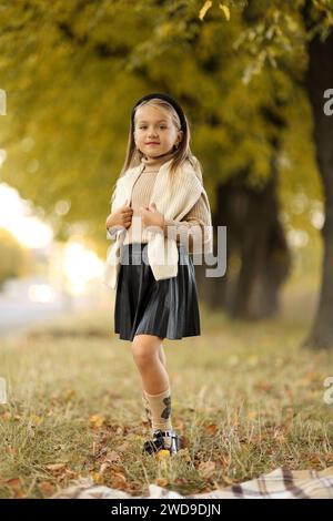 Kindertag. Fröhliches kleines Mädchen 5-6 Jahre alt posiert und lächelt draußen vor der Kamera und steht am Baum im Herbstpark. Stilvoller Zartpressdruck Stockfoto