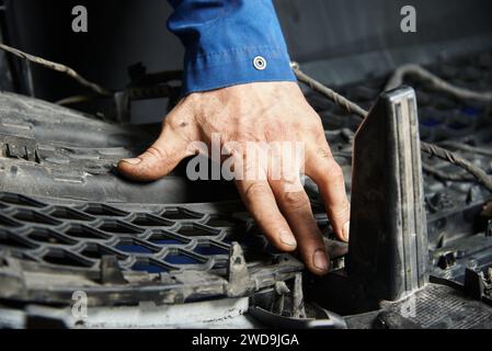 Hände des Meisters in Autos und verschiedenen Autoteilen. Automotor, Stoßfänger, Metallteile des Autos. Der Meister macht eine Autoreparatur in einer Autowerkstatt. Stockfoto