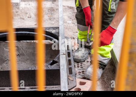Ein Straßenarbeiter repariert einen Gehbereich. Arbeiter fotografiert hinter einem Zaun Stockfoto