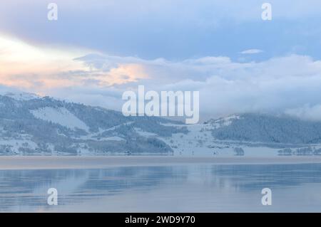 Ruhiger Winteruntergang über einem schneebedeckten Fjord mit aufsteigendem Nebel Stockfoto