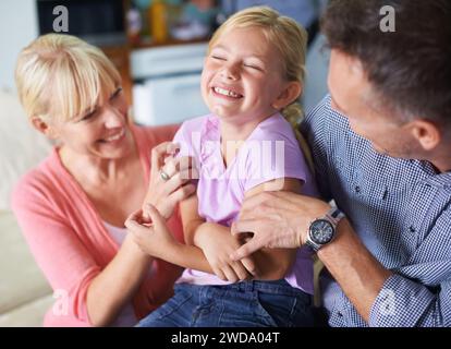 Mädchen, Eltern und Kitzeln für Spaß zu Hause, Sicherheit und Liebe in der Kindheit oder Glück. Familie, Tochter und Kind spielen im Urlaub, lächelnd Stockfoto