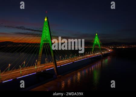 Aus der Vogelperspektive über die beleuchtete Megyeri-Brücke in einer seltenen weihnachtsdekoration mit atemberaubendem Sonnenuntergang im Hintergrund. Stockfoto