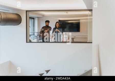 Ein junger Mann und eine junge Frau, die einen ruhigen Morgen mit Kaffee genießen und über ihre Pläne für den Tag in einem gemütlichen, sonnendurchfluteten, modernen Zuhause nachdenken. Stockfoto