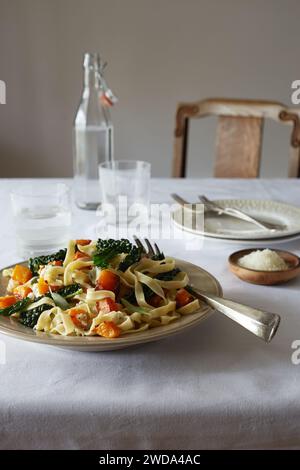 Tagliatelle mit gebratenem Butternusskürbis, Cavolo nero und Salbei, abgerundet mit Parmesan, serviert auf einem einfachen weißen Tisch. Stockfoto