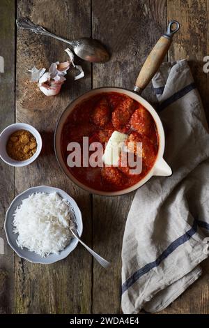 Fleischbällchen in reichhaltiger Tomatensauce mit geschmolzener Butter, serviert in einer rustikalen Pfanne mit weißem Reis, Knoblauch und Gewürzen auf Holztisch. Stockfoto
