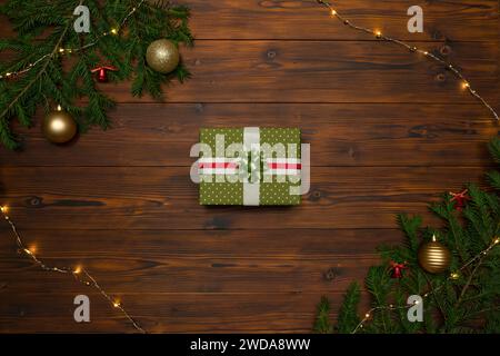 Weihnachtsgeschenkbox auf dunklem Holzhintergrund, eingerahmt von Tannenzweigen und Girlande. Stockfoto