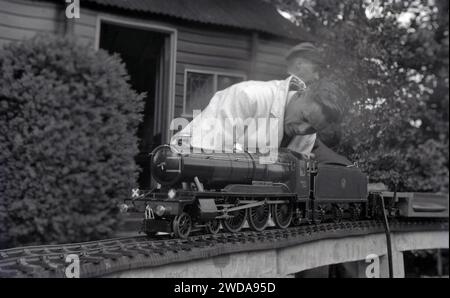 1950er Jahre, historisch, draußen im Garten der Field End Railway Co, England, Großbritannien, arbeitete ein Modelldampfeisenfreund in einem weißen Mantel an einer Miniatur-Dampfeisenbahn, der „County of Oxford“, einer GWR-Dampflokomotive, die 1947 in Betrieb ging. Stockfoto