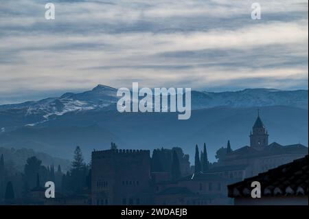 Blick auf die Türme der Alhambra bei einem nebeligen Winteraufgang mit den schneebedeckten Gipfeln der Sierra Nevada im Hintergrund Stockfoto