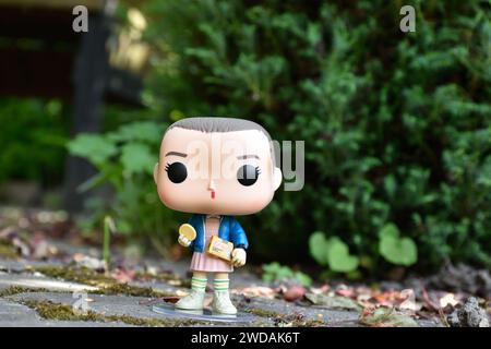 Funko Pop Actionfigur von Eleven mit Eggo-Waffeln aus der TV-Serie Stranger Things. Grüne Blätter, moosige Steinstraße, Frühlingsgarten. Stockfoto