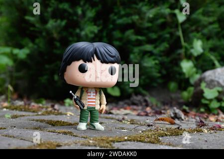 Funko Pop Actionfigur von Mike mit Walkie-Talkie aus der beliebten Horror-TV-Serie Stranger Things. Grüne Blätter, moosige Steinstraße, Frühlingsgarten. Stockfoto