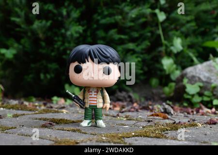 Funko Pop Actionfigur von Mike mit Walkie-Talkie aus der beliebten Horror-TV-Serie Stranger Things. Grüne Blätter, moosige Steinstraße, Frühlingsgarten. Stockfoto