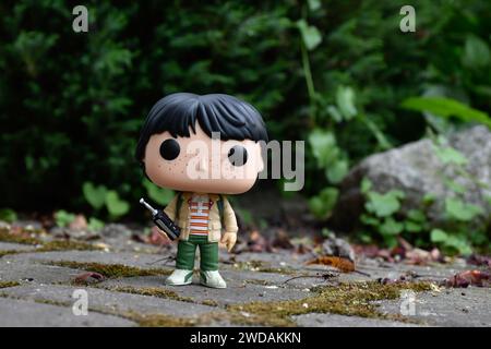 Funko Pop Actionfigur von Mike mit Walkie-Talkie aus der beliebten Horror-TV-Serie Stranger Things. Grüne Blätter, moosige Steinstraße, Frühlingsgarten. Stockfoto