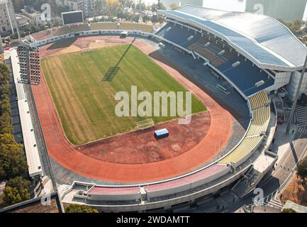 Ein riesiges, offenes Sportfeld mit einer roten Start- und Landebahn, die ein normales Fußballfeld umgibt und von Sonnenlicht beleuchtet wird. Stockfoto