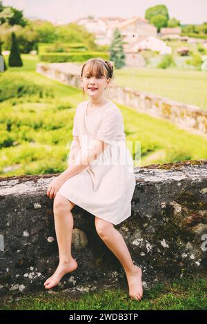 Hübsches kleines Mädchen, das an einem schönen Sommertag in einem wunderschönen Garten spielt, in einem weißen Kleid im Vintage-Stil Stockfoto