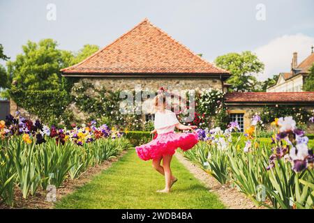 Süßes kleines Mädchen, das in einem wunderschönen Blumengarten an einem schönen sonnigen Sommertag tanzt und einen hellrosa Tutu-Rock trägt Stockfoto