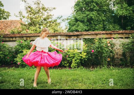 Süßes kleines Mädchen, das in einem wunderschönen Blumengarten an einem schönen sonnigen Sommertag tanzt und einen hellrosa Tutu-Rock trägt Stockfoto
