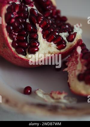 Vertikale Nahaufnahme eines offenen, leuchtend roten Granatapfels auf einer beigefarbenen Platte. Stockfoto