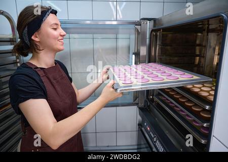 Der fröhliche junge Bäcker backt Kekse in der Bäckereiküche Stockfoto
