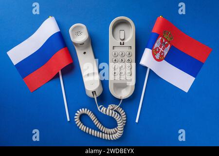 Altes Telefon und zwei Flaggen auf blauem Hintergrund, Konzept zum Thema Telefongespräche zwischen Serbien und Russland Stockfoto