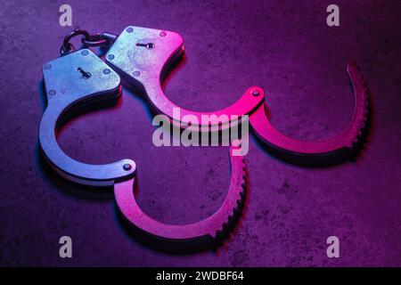 Offene Handschellen auf dunklem Hintergrund, beleuchtet mit einem farbigen gemischten Rot- und Blaulicht Stockfoto