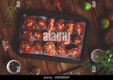 Zubereitung von Tomatenkonserven. Halbierte Tomaten mit Thymian und Knoblauch auf Backblech. Blick von oben Stockfoto