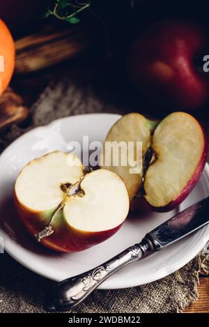 Zwei Hälften von rotem Apfel auf weißem Teller mit Vintage Messer in rustikaler Umgebung Stockfoto