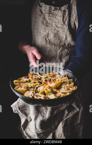 Der Küchenchef hält eine Pfanne mit gebackenen Jumbo-Shells-Pasta, gefüllt mit Hackfleisch, Spinat und Käse Stockfoto