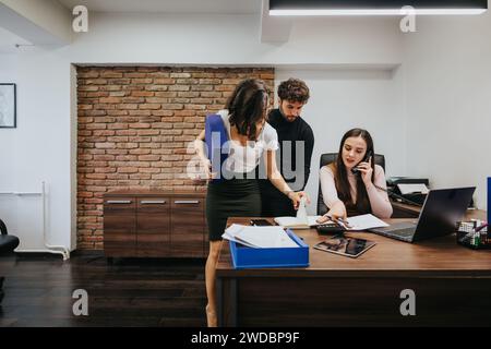 Drei Profis in einem Büro, einer telefonisch und zwei diskutieren Dokumente und zeigen Teamarbeit und Zusammenarbeit. Stockfoto