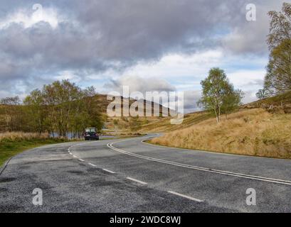 Eine kurvige Landstraße schlängelt sich mit einem Bus durch eine herbstliche Landschaft. Schottland, Großbritannien Stockfoto